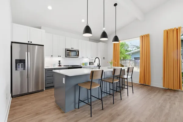 a kitchen with stainless steel appliances granite countertop a stove a refrigerator a microwave a dining table and chairs with wooden floor