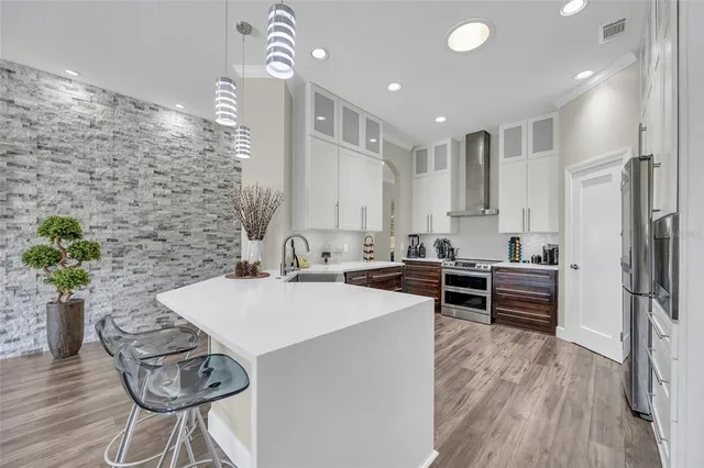 a kitchen with stainless steel appliances kitchen island granite countertop a refrigerator a stove a sink and white cabinets with wooden floor