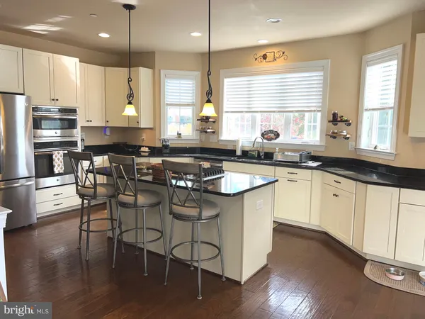 a kitchen with stainless steel appliances granite countertop a sink a stove a refrigerator and island with wooden floor