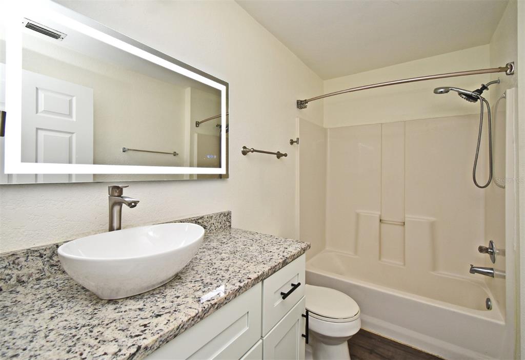 5467 Vineland Road, Unit 6308 Orlando, FL 32811 - Photo 6 of 39 a bathroom with a granite countertop sink a toilet mirror and shower