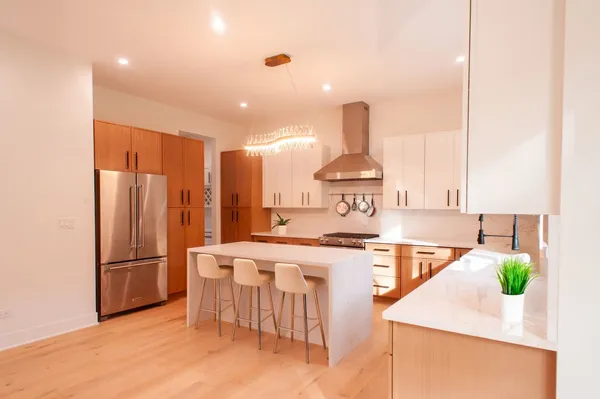 a kitchen with stainless steel appliances kitchen island granite countertop a refrigerator a stove and a wooden floors