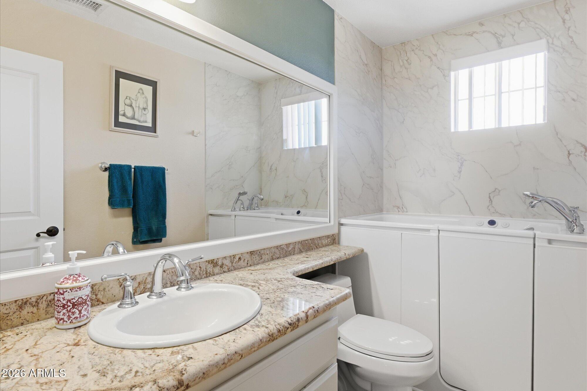 3895 North 150th Lane Goodyear, AZ 85395 - Photo 19 of 34 a bathroom with a granite countertop sink a toilet and a mirror