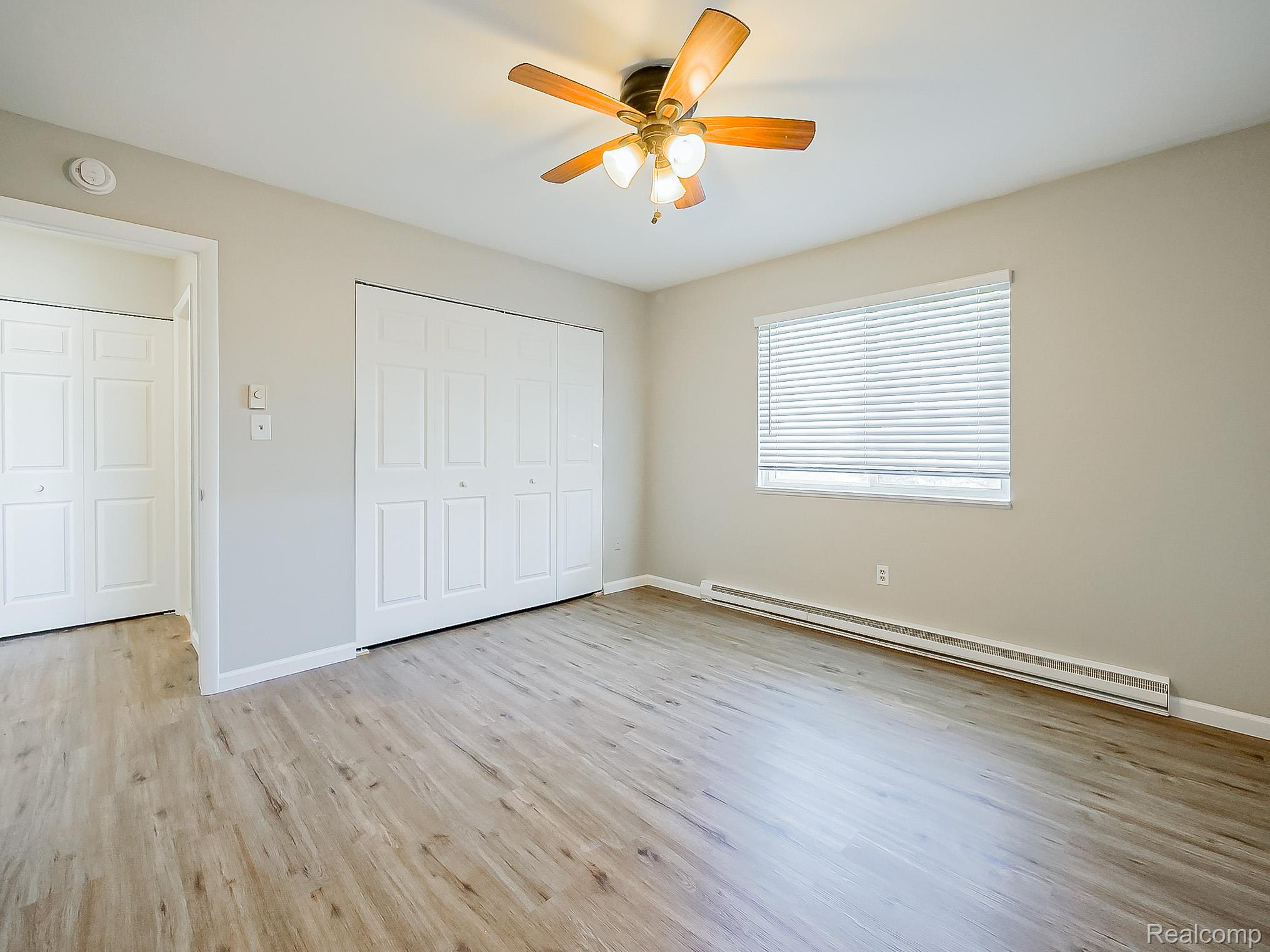 125 East Van Riper Road, Unit 5 Fowlerville, MI 48836 - Photo 14 of 23 Unfurnished bedroom with a baseboard heating unit, light wood-style floors, a closet, and a ceiling fan