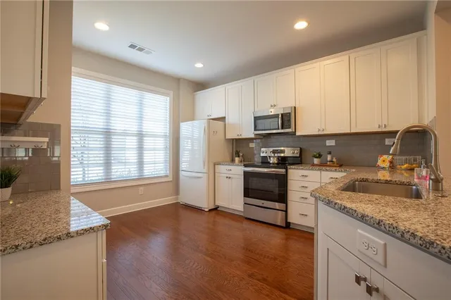 a kitchen with stainless steel appliances granite countertop a stove a sink a refrigerator and white cabinets with wooden floor