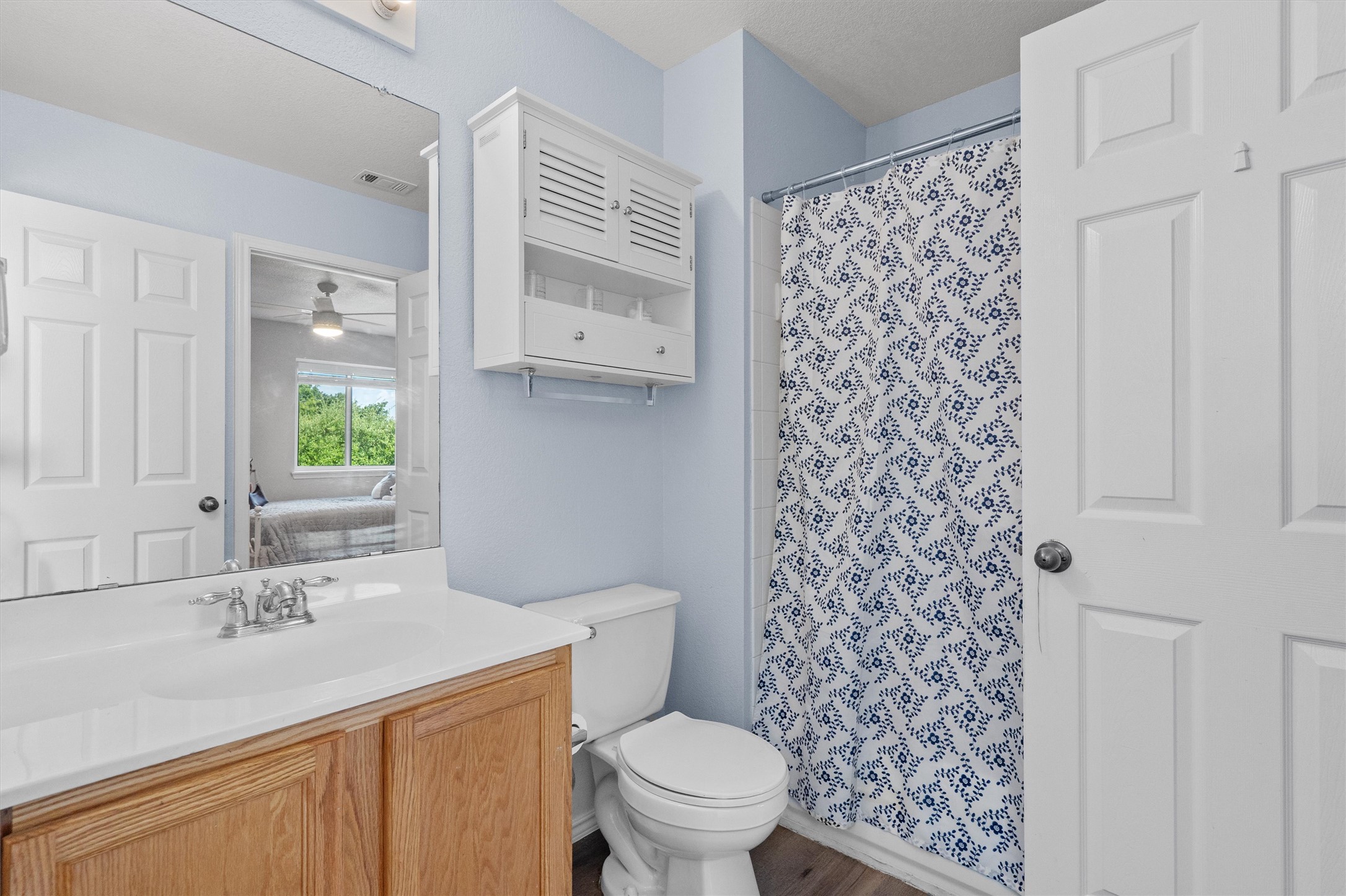 1833 Thompson Trail Round Rock, TX 78664 - Photo 28 of 40 A cheerful bathroom features a wooden vanity with ample storage and a refreshing blue-patterned shower curtain.