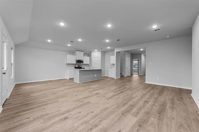 a view of an empty room with wooden floor kitchen appliances and a window