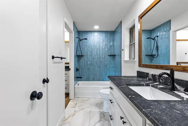 a bathroom with a granite countertop sink a toilet a mirror and shower