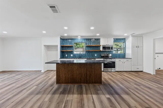 a large kitchen with stainless steel appliances granite countertop a stove and a wooden floors