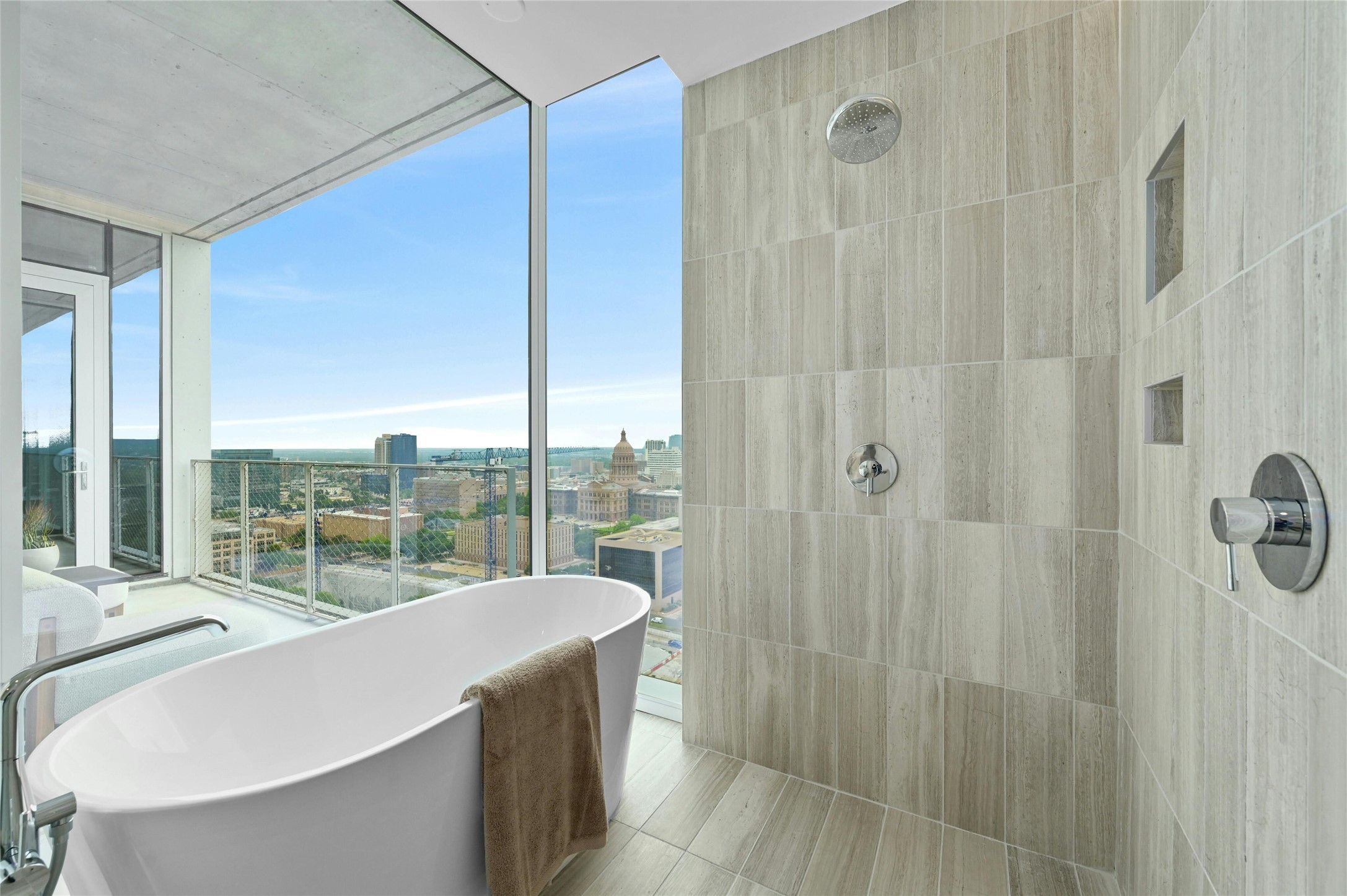 313 West 17th Street, Unit 1807 Austin, TX 78701 - Photo 6 of 39 The primary bathroom features a bathtub with tiles that resemble wood, adding a touch of natural elegance. It includes a separate shower area and a panoramic view window with a glass panel, offering scenic vistas and enhancing the bathroom's ambiance.