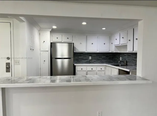 a kitchen with stainless steel appliances granite countertop a refrigerator a sink and white cabinets