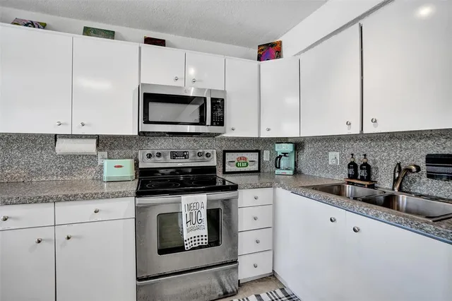a kitchen with granite countertop white cabinets white stainless steel appliances and a sink