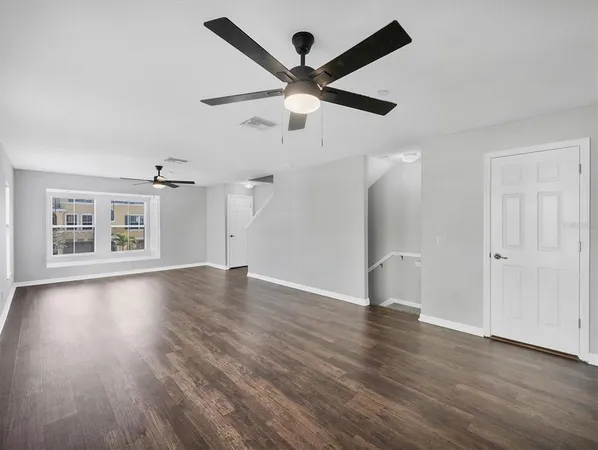 a view of an empty room with wooden floor and a ceiling fan