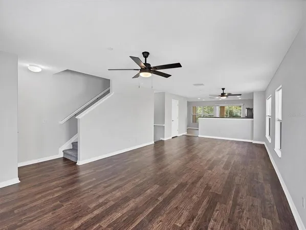 a view of an empty room with wooden floor and a ceiling fan