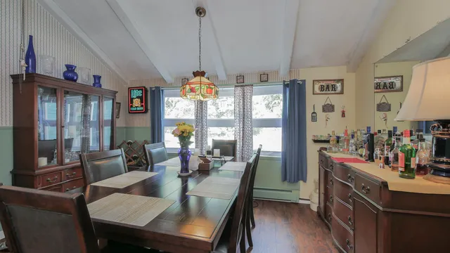 a view of a dining room and livingroom with furniture wooden floor a rug a flat screen tv a rug and a large window