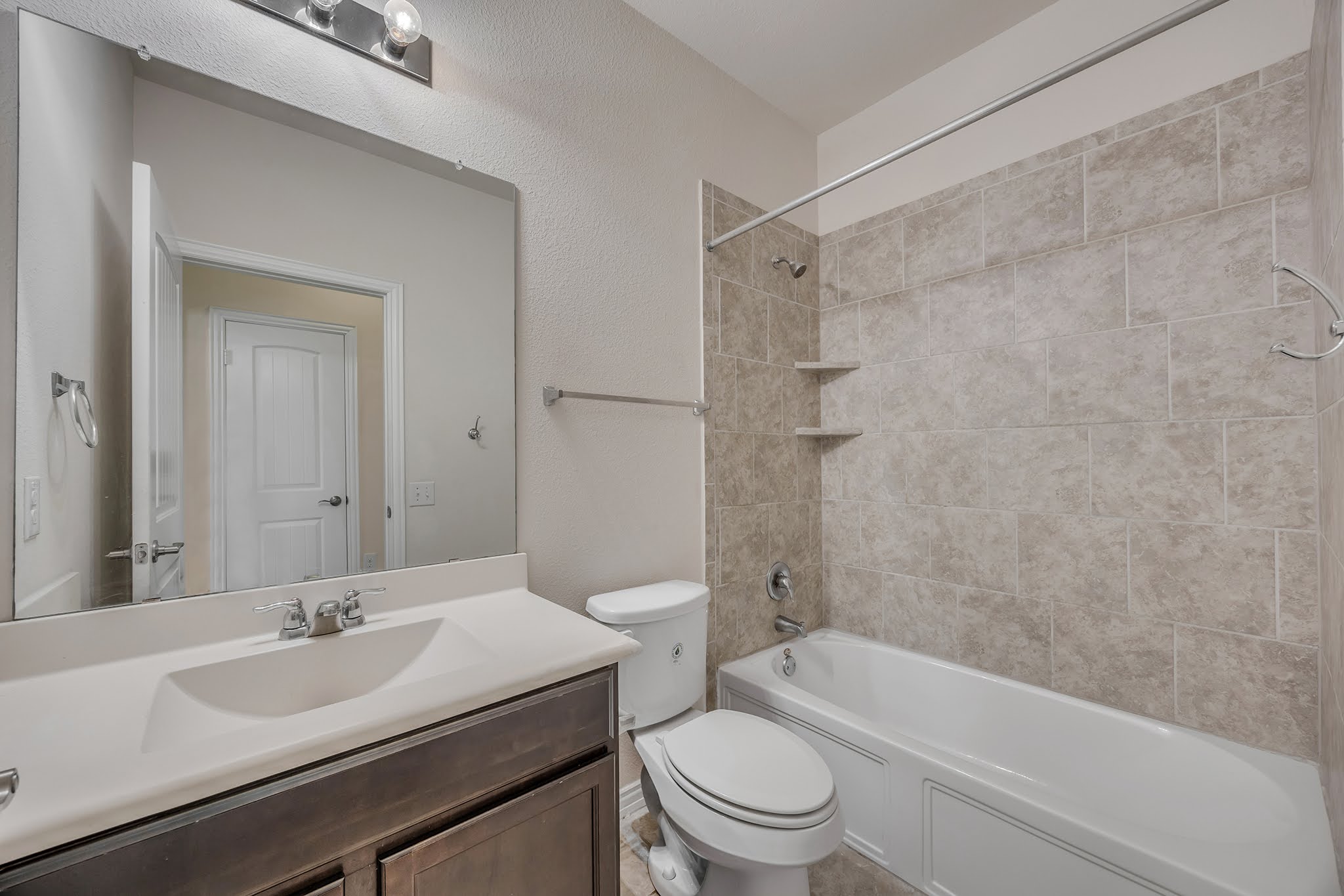 7212 Vail Ridge Street Austin, TX 78744 - Photo 11 of 26 A well-appointed bathroom offers a clean vanity, full mirror, and tiled shower with integrated shelving.