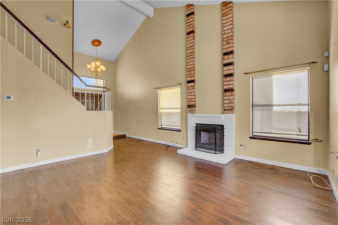 6440 Hartwood Road Las Vegas, NV 89108 - Photo 7 of 59 A spacious living room features soaring ceilings, a brick fireplace, and durable hardwood-style flooring.