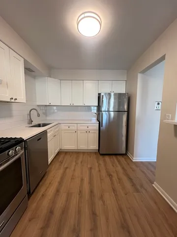 a kitchen with a white cabinets a sink dishwasher a refrigerator and wooden floor