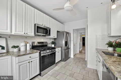a kitchen with stainless steel appliances granite countertop a stove a sink dishwasher a refrigerator and a microwave oven with white cabinets