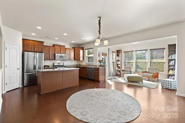 a kitchen with stainless steel appliances kitchen island granite countertop a refrigerator a oven a couches with wooden floor