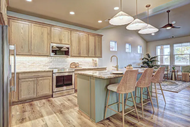 a kitchen with stainless steel appliances granite countertop a stove top oven a sink a dining table and chairs with wooden floor