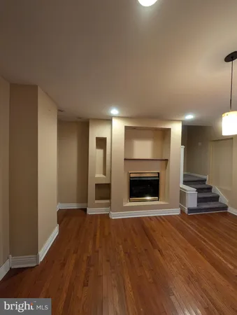 a view of an empty room with wooden floor fire place and a kitchen