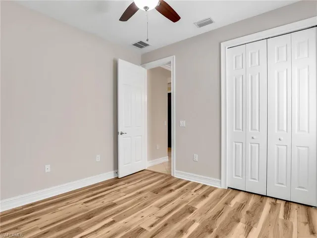 an empty room with wooden floor chandelier fan and windows