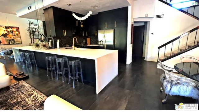 a view of living room kitchen with stainless steel appliances kitchen island granite countertop a table chairs and a wooden floor
