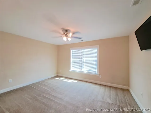 an empty room with chandelier fan and windows