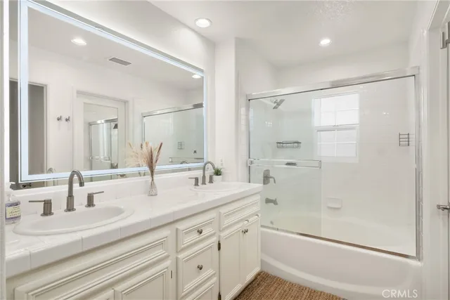 a bathroom with double vanity sink and mirror with shower