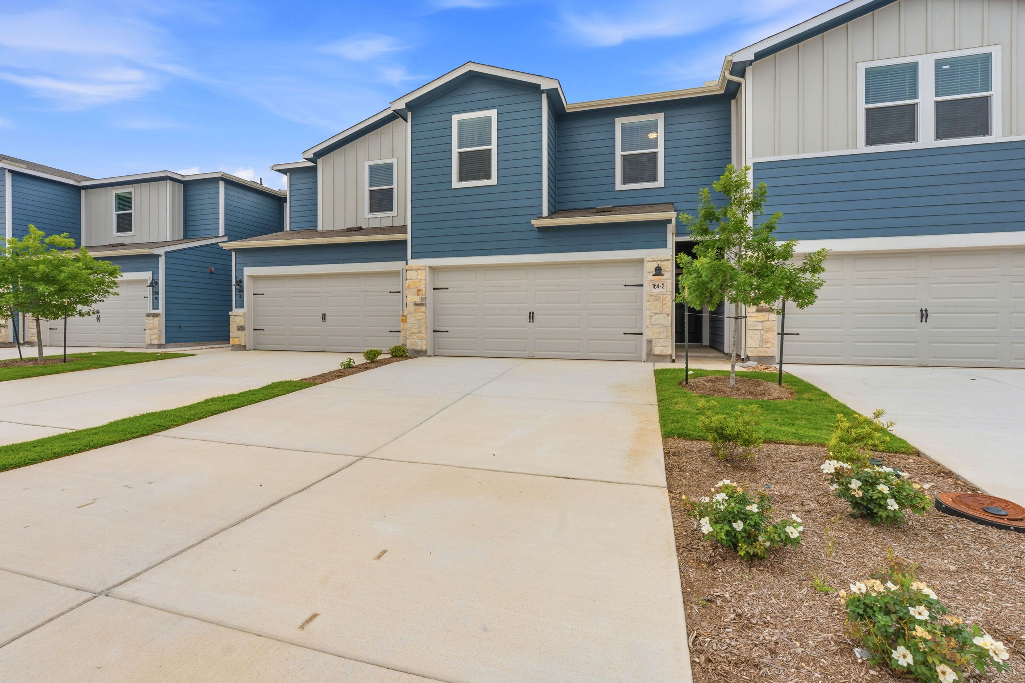 164 Cinnabar Lane, Unit 2 Kyle, TX 78640 - Photo 1 of 21 Modern townhome exterior featuring blue siding, light vertical siding accents, stone veneer columns, a two-car garage, and a concrete driveway