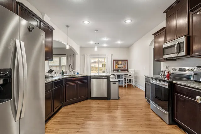 a kitchen with stainless steel appliances kitchen island granite countertop a refrigerator a stove top oven and white cabinets with wooden floor