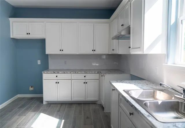 a kitchen with granite countertop a sink dishwasher a stove and white cabinets with wooden floor