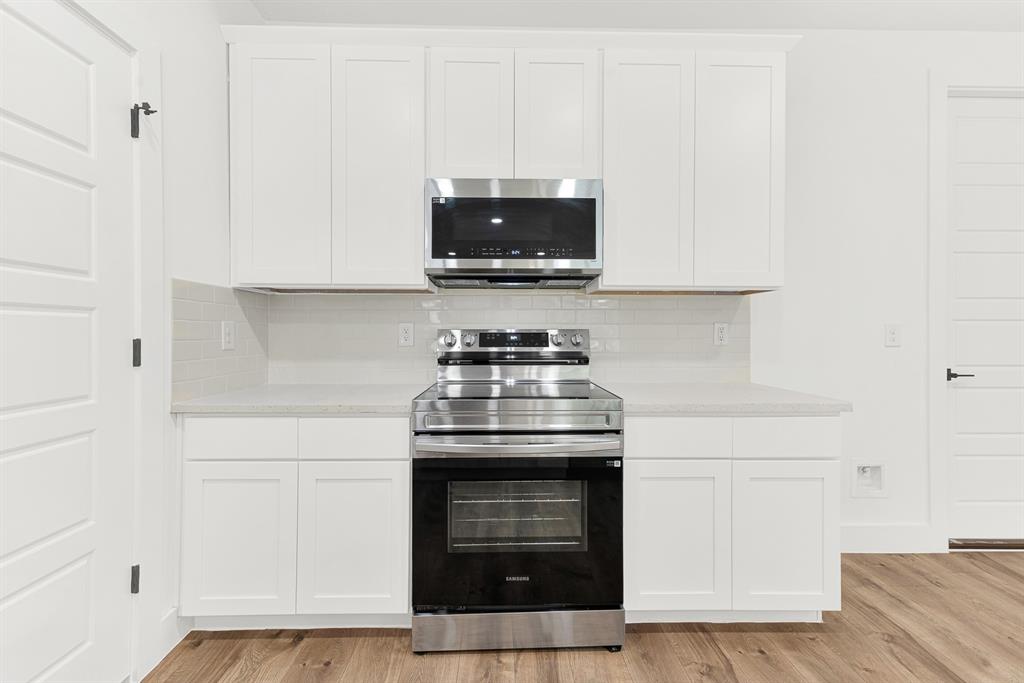 9471 Timberleaf Drive Dallas, TX 75243 - Photo 7 of 39 Kitchen featuring white shaker-style cabinetry, stainless steel range and microwave, light-toned countertop, subway tile backsplash, and wood-finish flooring