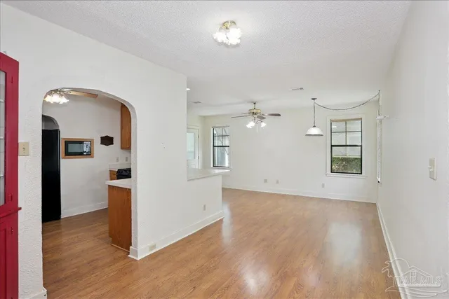 an empty room with wooden floor chandelier fan and windows