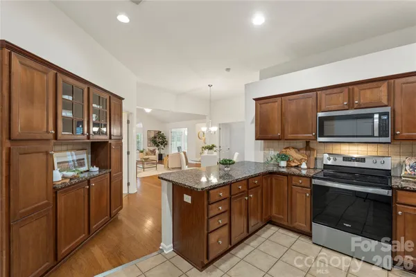 a kitchen with stainless steel appliances granite countertop a stove top oven a sink dishwasher a dining table and chairs with wooden floor