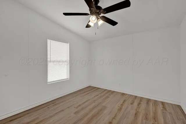 an empty room with wooden floor ceiling fan and windows