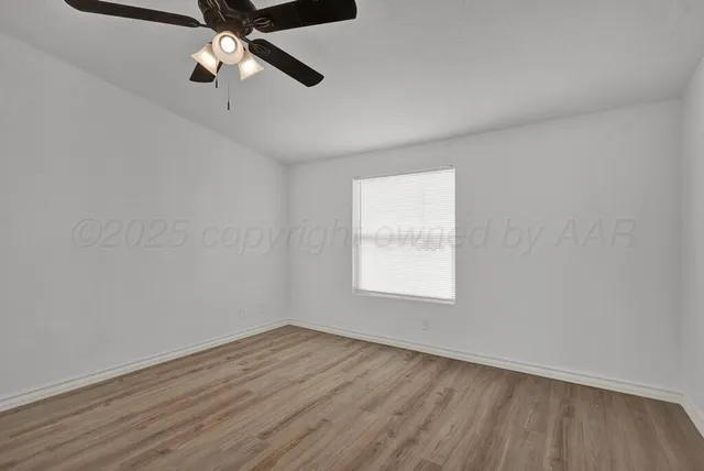 an empty room with wooden floor ceiling fan and windows