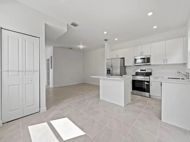 a kitchen with granite countertop a refrigerator oven a sink and white cabinets