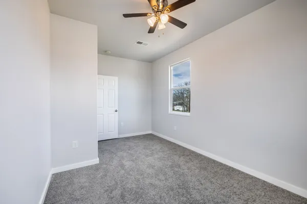 an empty room with chandelier fan and windows