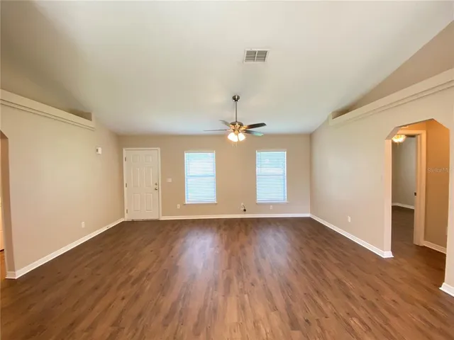 an empty room with wooden floor ceiling fan and windows