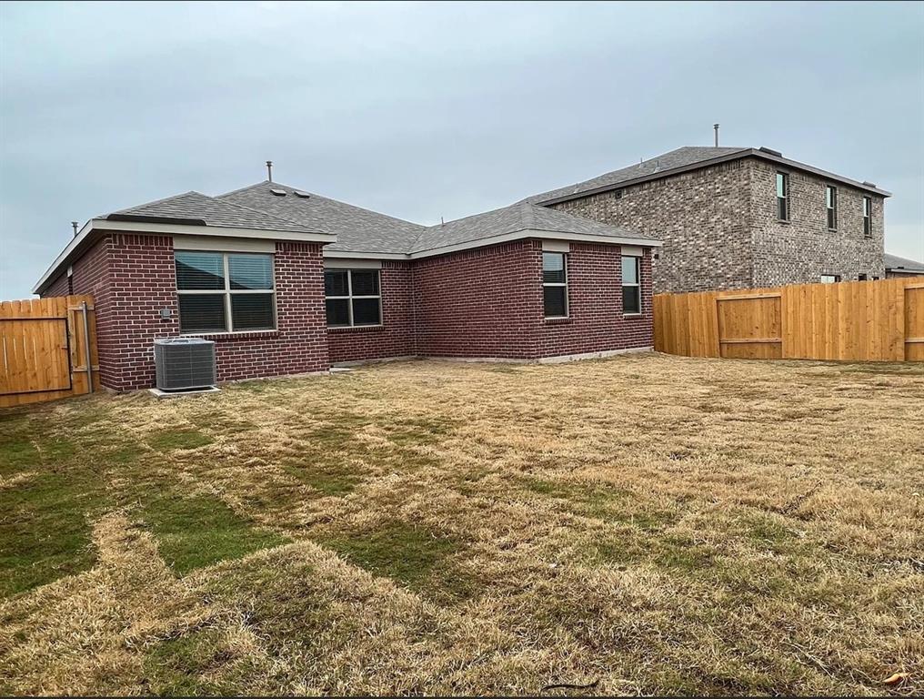 2013 Emma Court Anna, TX 75409 - Photo 18 of 20 Expansive backyard featuring a full wood privacy fence, red brick exterior, multiple windows with dark frames, and a visible HVAC unit