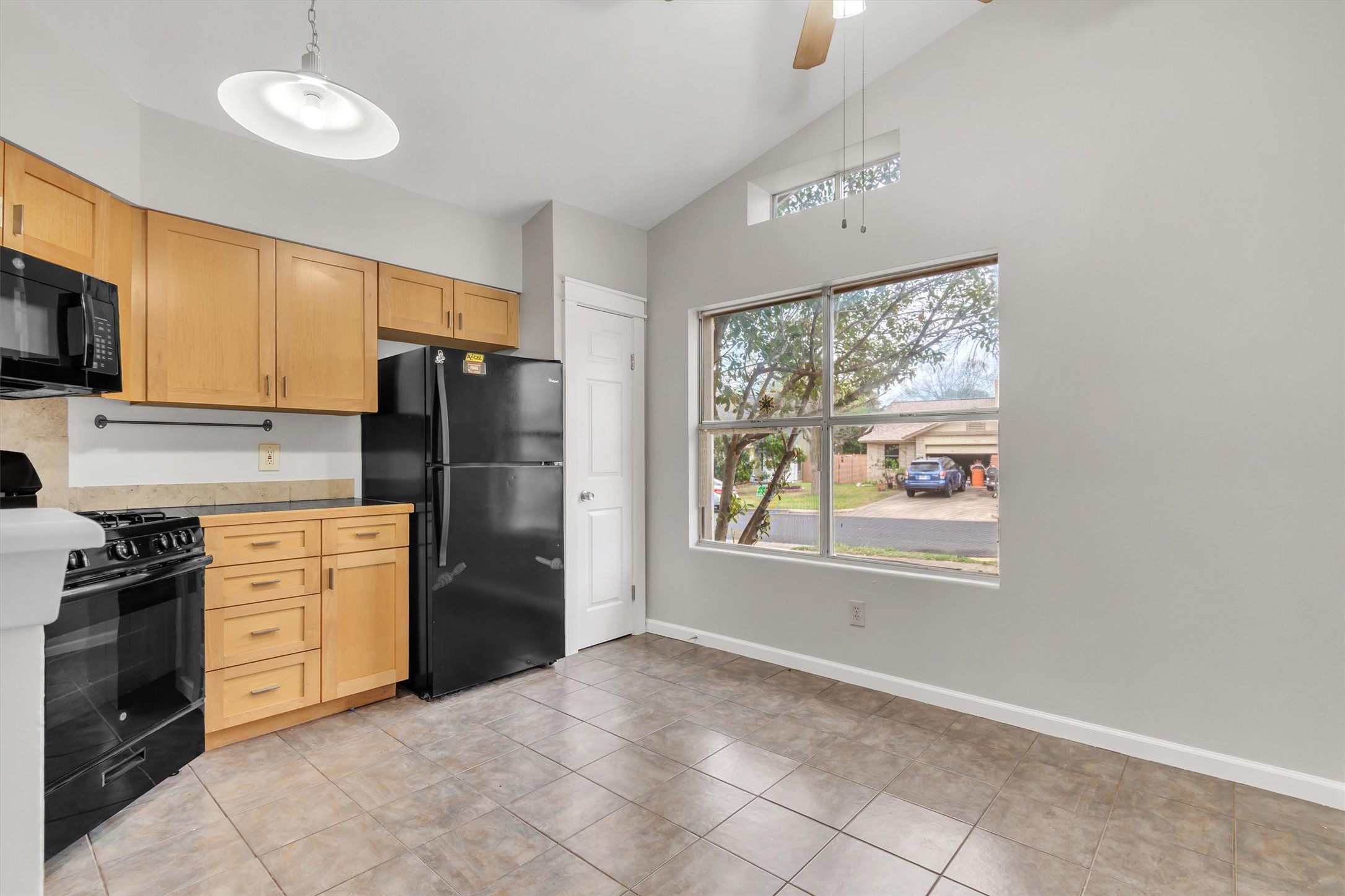 720 Decker Prairie Drive Austin, TX 78748 - Photo 7 of 21 Kitchen featuring light wood finish cabinets, black appliances, vaulted ceiling, ceiling fan, and hanging light fixtures