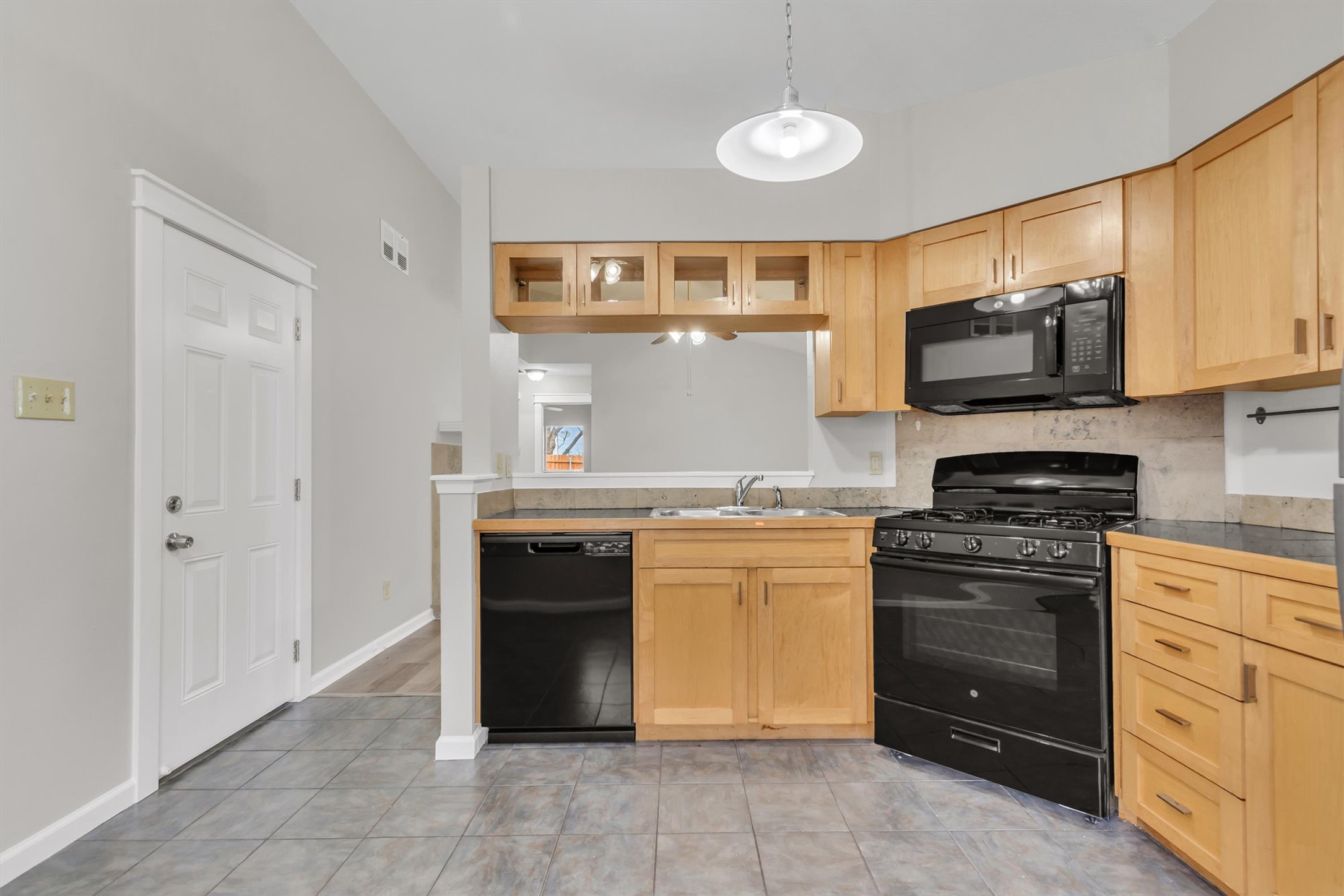 720 Decker Prairie Drive Austin, TX 78748 - Photo 8 of 21 Kitchen featuring black appliances, light wood finish cabinetry, hanging light fixtures, and glass fronted cabinets