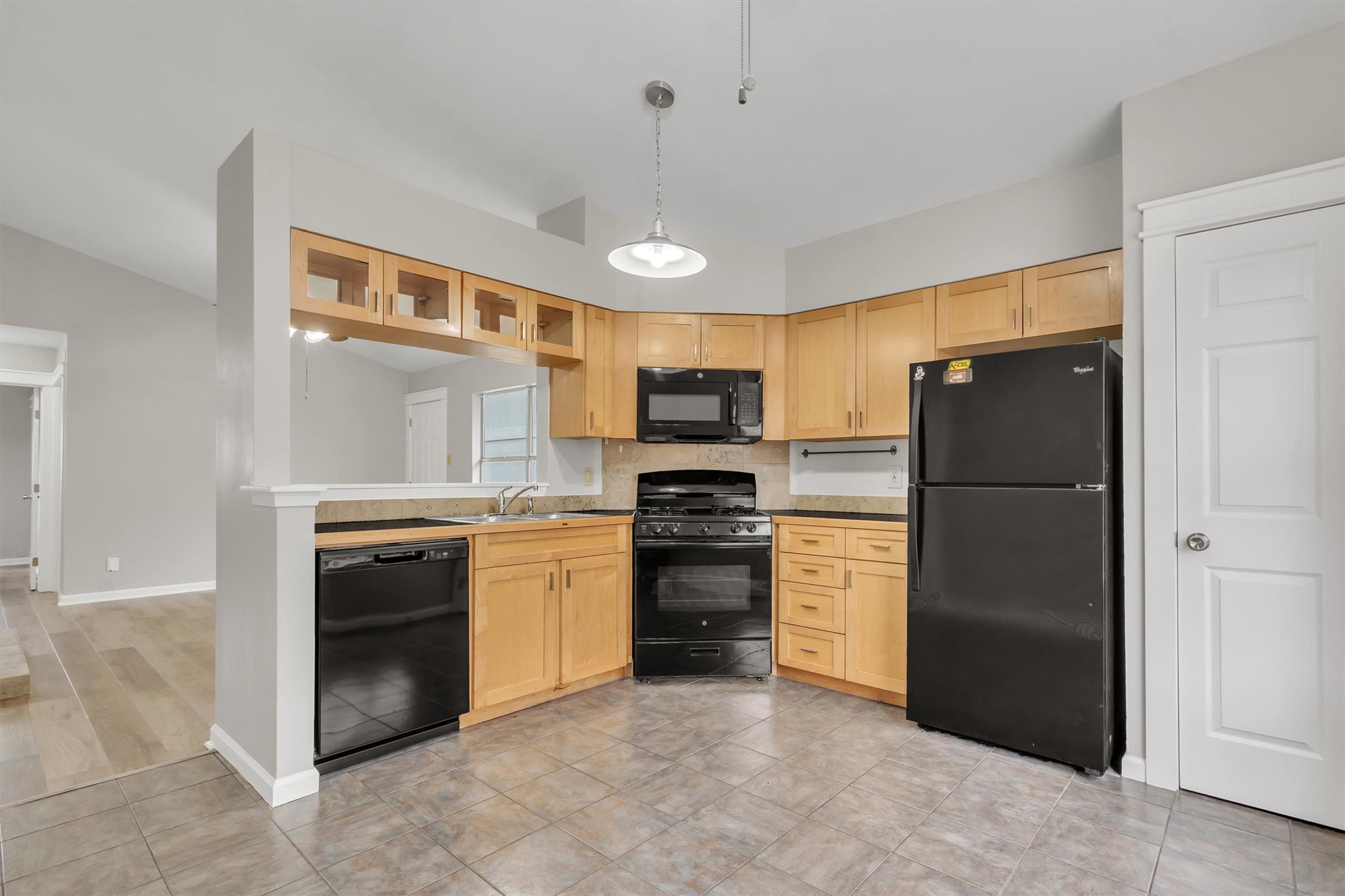 720 Decker Prairie Drive Austin, TX 78748 - Photo 9 of 21 Kitchen featuring black appliances, light wood finish cabinetry, pendant lighting, glass insert cabinets, and light tile patterned floors