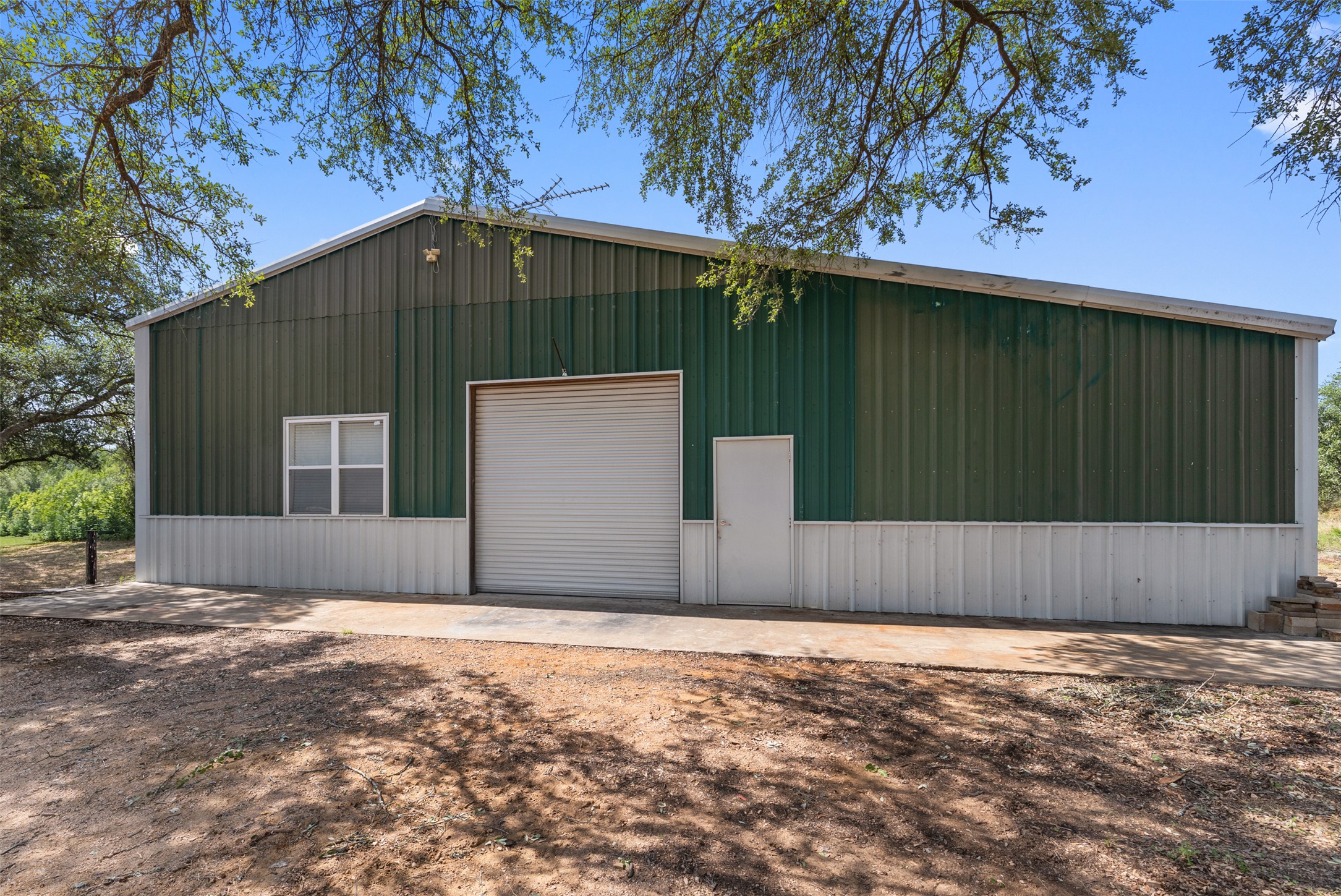 764 Stubbs Road Johnson City, TX 78636 - Photo 7 of 29 A spacious workshop with a roll-up door and ample exterior space, nestled among mature trees.