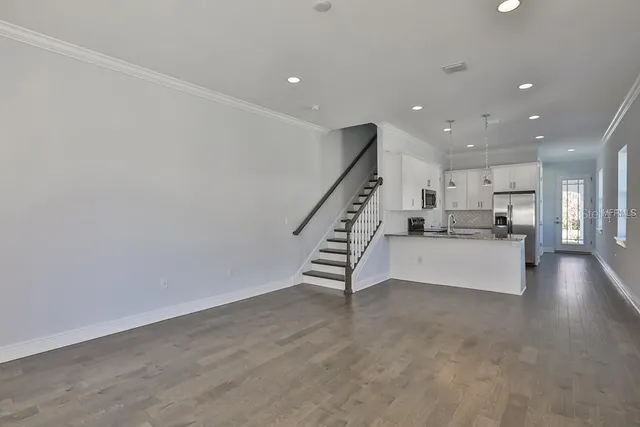 a view of an empty room with wooden floor stairs and a kitchen view