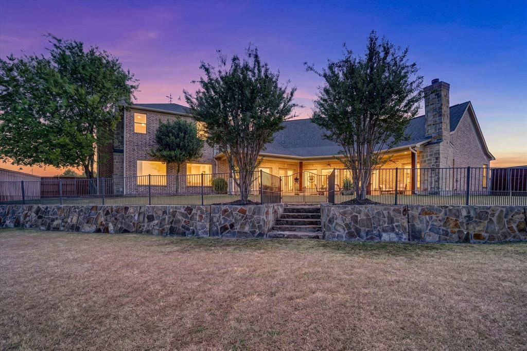 100 Canyon Ridge Trail Aledo, TX 76008 - Photo 32 of 38 Elegant stone-front residence showcasing arched entryways, multiple illuminated windows, and mature landscaping with specimen trees framing the facade