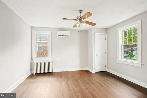 an empty room with wooden floor windows and fan