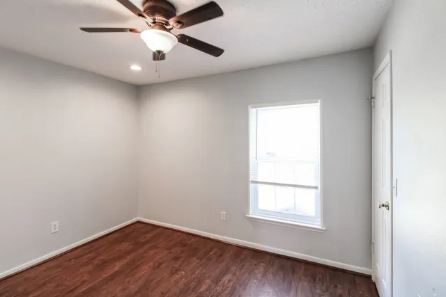 an empty room with wooden floor chandelier fan and windows