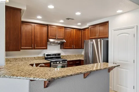 a kitchen with stainless steel appliances granite countertop a refrigerator a stove and a sink with wooden cabinets